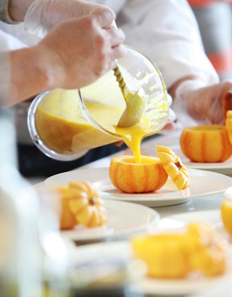Chef performing culinary artistry by pouring vibrant pumpkin soup in decorative pumpkins.