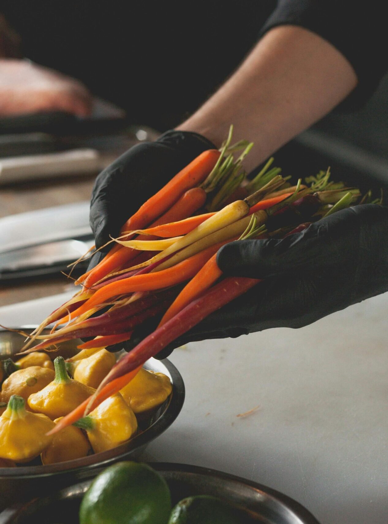 Chef wearing gloves handles fresh carrots and patty pan squash, highlighting preparation